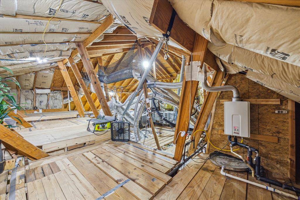 The attic space is lighted and the ductwork is secured with netting.  There is a  tankless water heater too. The area appears unfinished but spacious, offering potential for storage or future renovations.