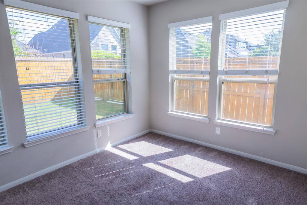 Bright and inviting room with multiple windows, offering plenty of natural light and views of the fenced backyard. Neutral walls and cozy carpet create a warm atmosphere.
