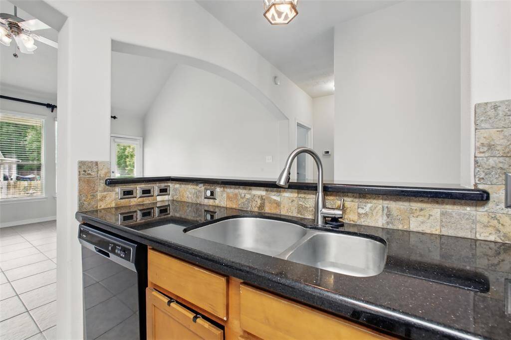 This view from the kitchen highlights the functional layout and open-concept design. The double-basin stainless steel sink is set in polished granite countertops, complemented by a natural stone backsplash. The raised breakfast bar offers a great space for casual seating or serving, while the arched opening maintains a connection to the living area—perfect for entertaining or everyday family living.