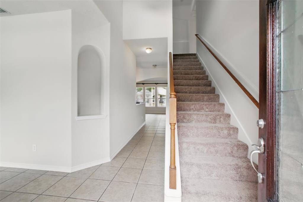 This welcoming entryway features neutral tile flooring and a softly arched wall niche that adds a custom touch. A carpeted staircase with wood railing leads to the second level, while the open sightline to the back of the home fills the space with natural light. A bright and functional layout sets the tone for the rest of the home.