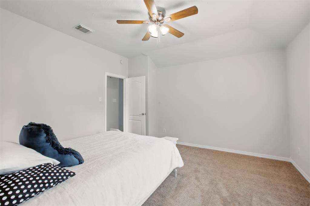 This comfortable secondary bedroom offers soft carpet underfoot, a neutral color palette, and a ceiling fan with lighting for year-round comfort. A large window lets in natural light while providing a peaceful view, and the closet door hints at ample storage. A cozy and quiet retreat for family or guests!