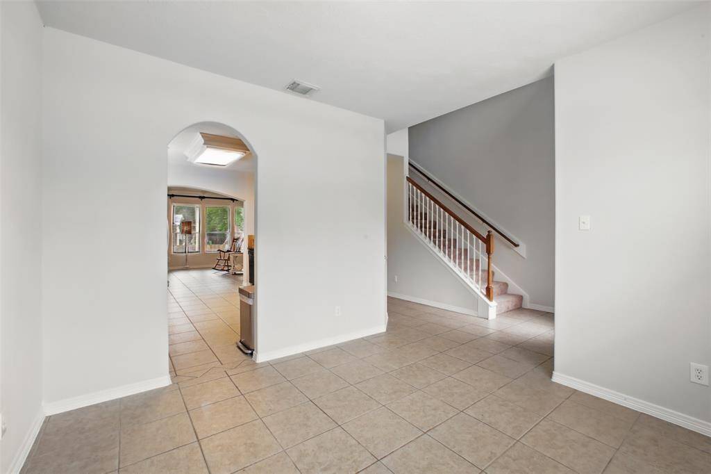 This inviting entryway features neutral tile flooring that flows seamlessly into the main living areas. A charming arched doorway leads into a light-filled space with a wall of windows overlooking the backyard. The staircase with white spindles and a wood handrail adds a classic touch, and the soft wall tones create a clean, welcoming feel. Perfect for a variety of decorating styles!