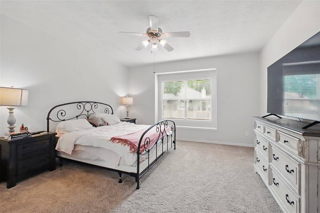 Spacious primary suite with plush carpet, large window for natural light, and neutral tones throughout. Features a ceiling fan, walk-in closet, and direct access to the en-suite bath. A peaceful retreat to unwind in comfort.