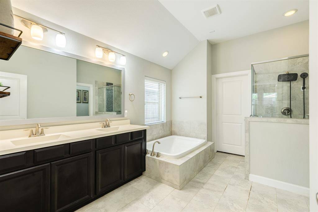 primary bath has double vanities, soaking tub with a window with blinds a walk in closet and separate shower