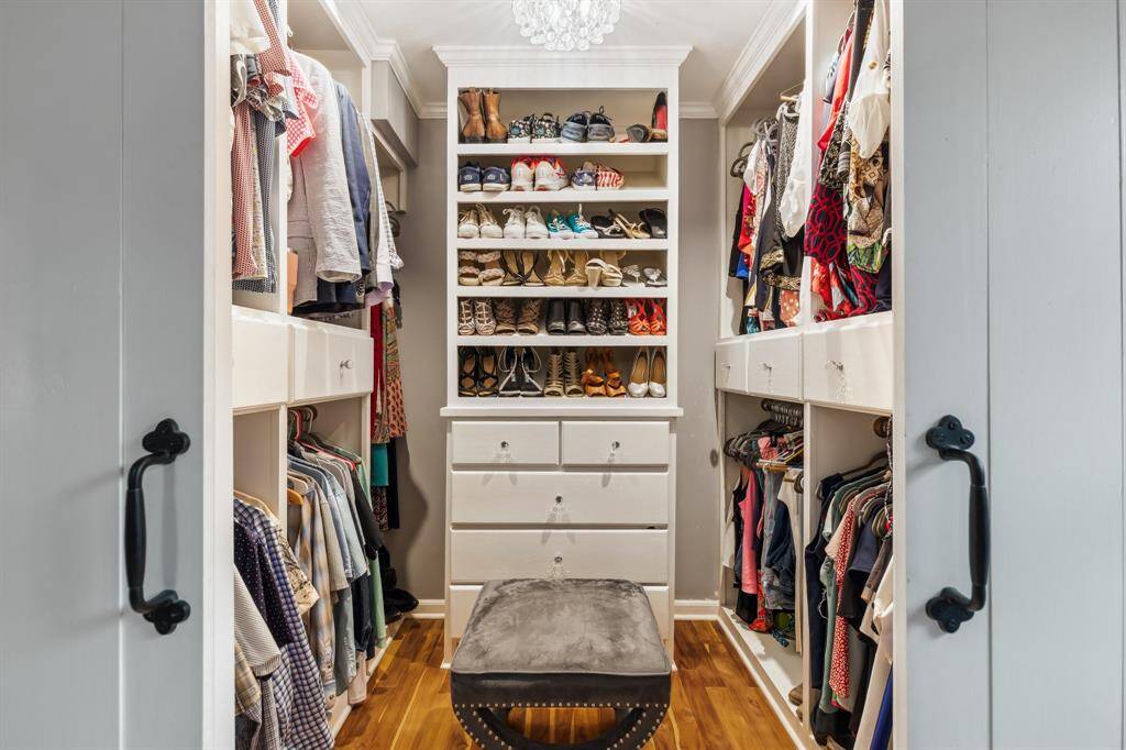 Custom-designed for optimal organization, this walk-in closet includes built-in drawers, shelving, and hanging space, all finished with upgraded hardware and a statement chandelier.