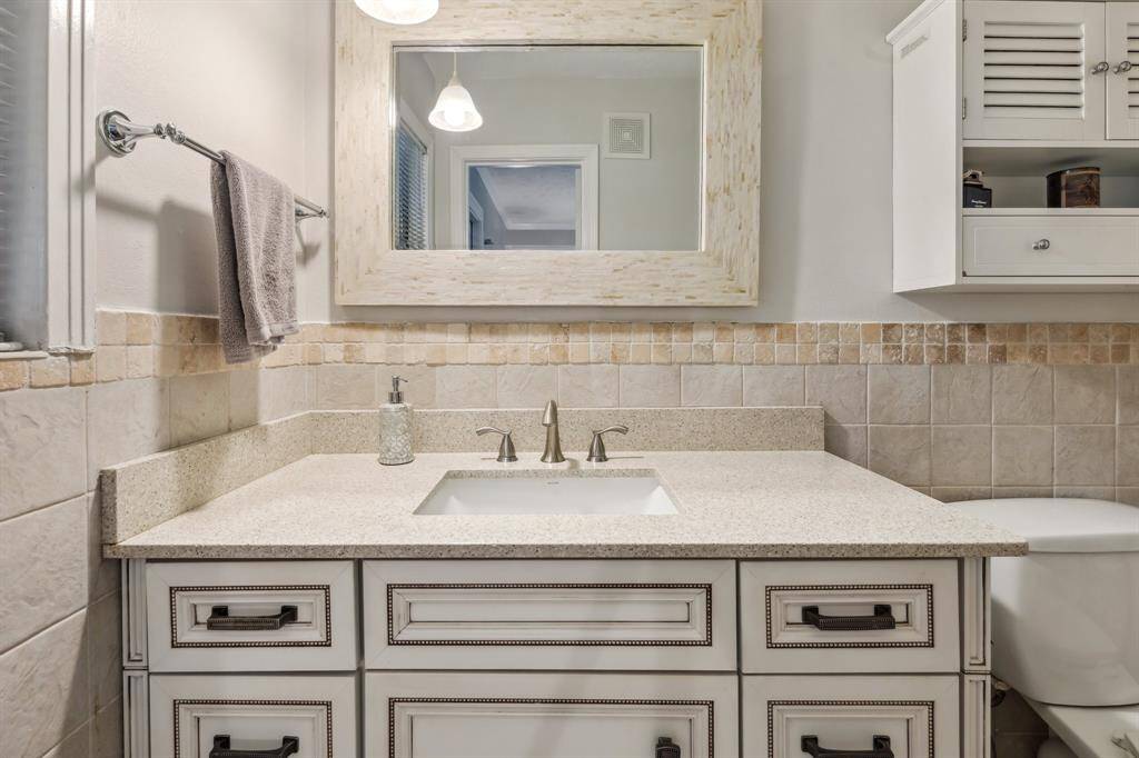 The en-suite bath offers a stylish vanity with detailed cabinetry, under-mount sink, and mosaic tile accents that pair beautifully with the soft, neutral finishes.