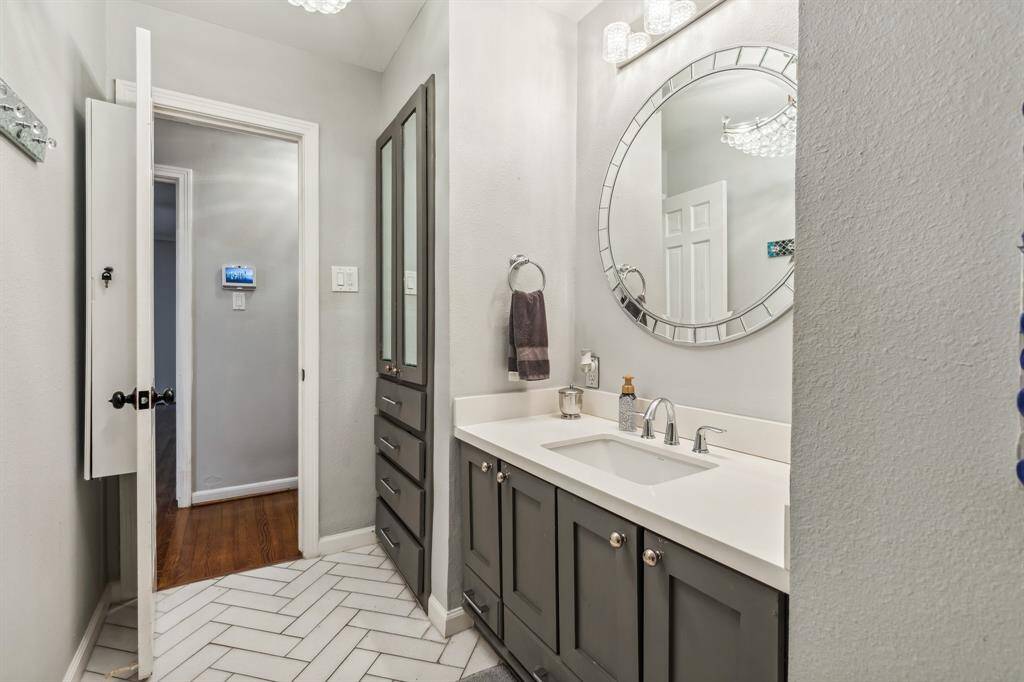 Updated with stylish finishes, this secondary bath features a sleek vanity with ample storage, quartz-style counters, a designer mirror, and modern lighting—all set atop herringbone tile flooring for added flair.