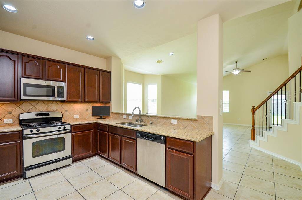 This photo showcases a modern kitchen with stainless steel appliances, dark wood cabinetry, and a tiled backsplash. The open layout connects to a bright living area.