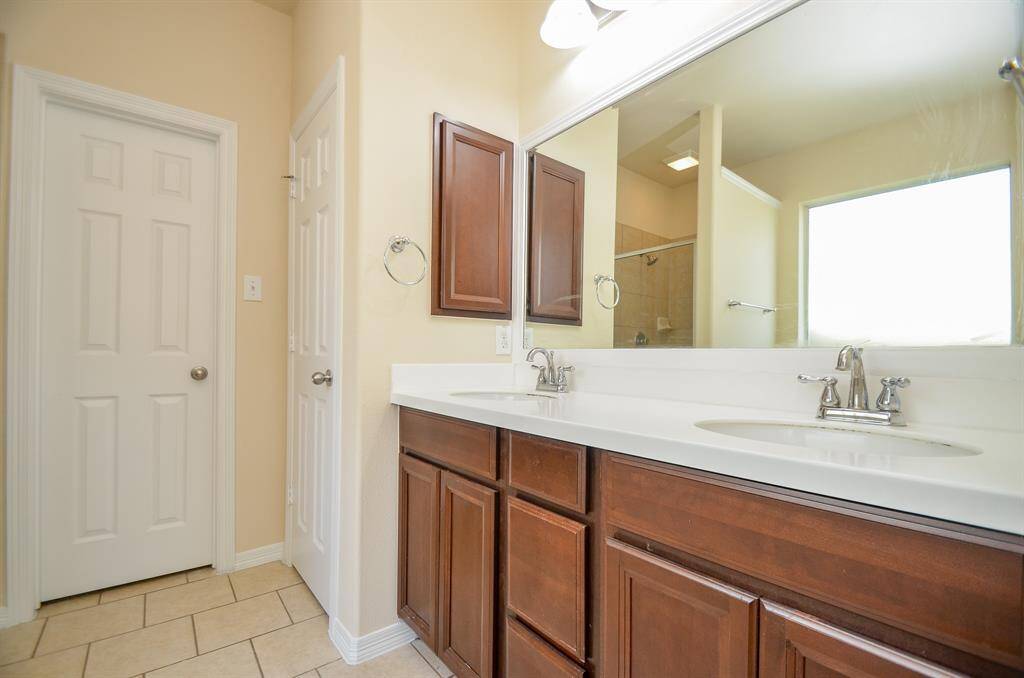 This primary bathroom features a double vanity with elegant dark wood cabinets, a large mirror, and modern fixtures. It has a neutral color palette and tiled floor, offering a spacious and bright atmosphere.