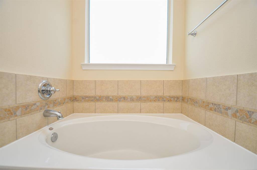 This primary bathroom features a spacious bathtub with elegant tile detailing and a bright window, creating a serene and inviting atmosphere.