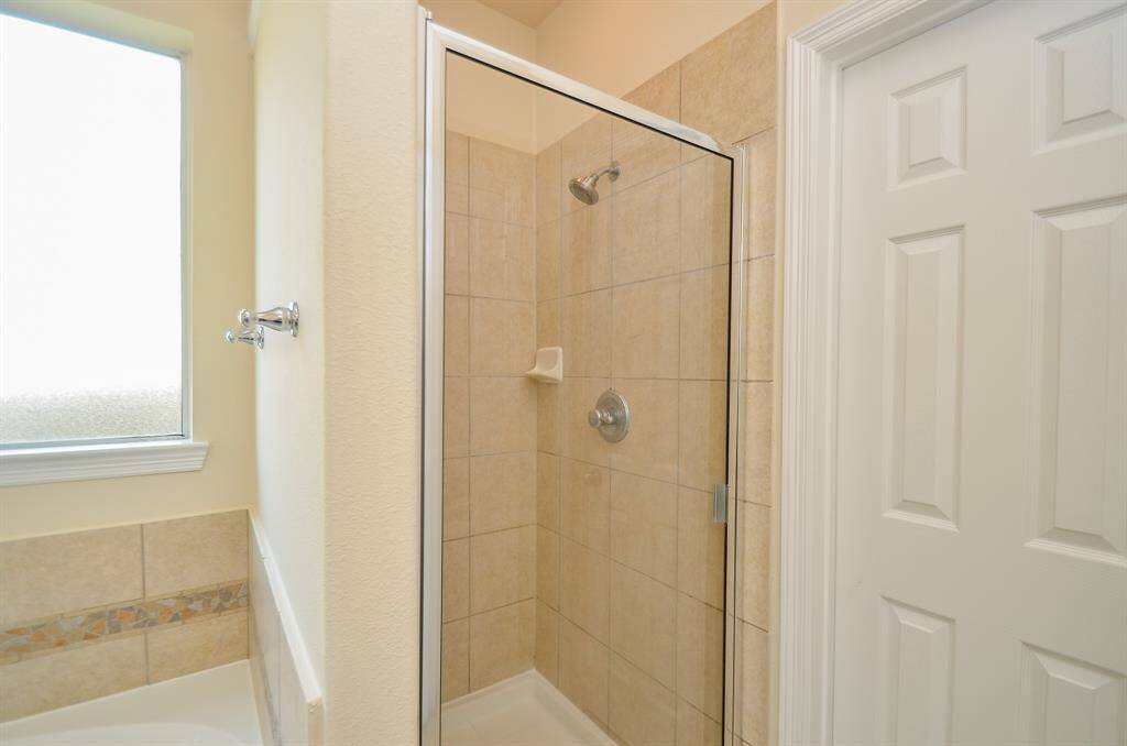 This photo shows a clean, modern bathroom with a tiled walk-in shower featuring a glass door. There's a frosted window for natural light and privacy, and a bathtub with decorative tile accents.