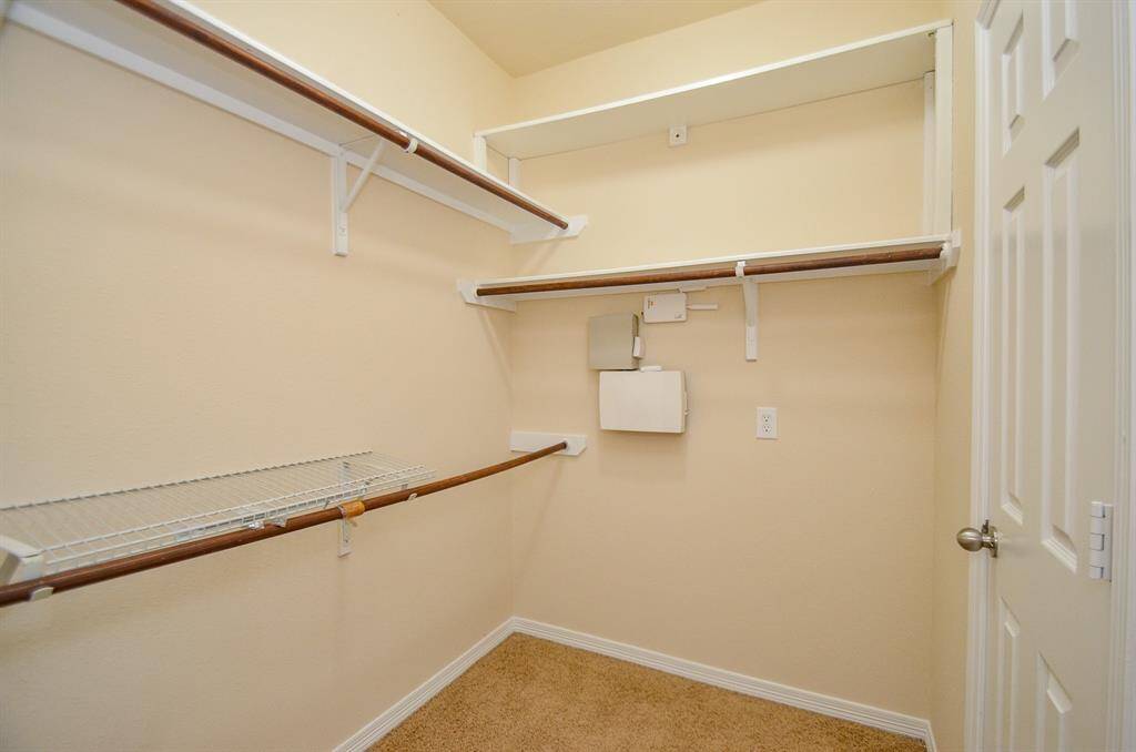 This photo shows a spacious walk-in closet with carpeted flooring, and multiple shelves and rods for ample storage.