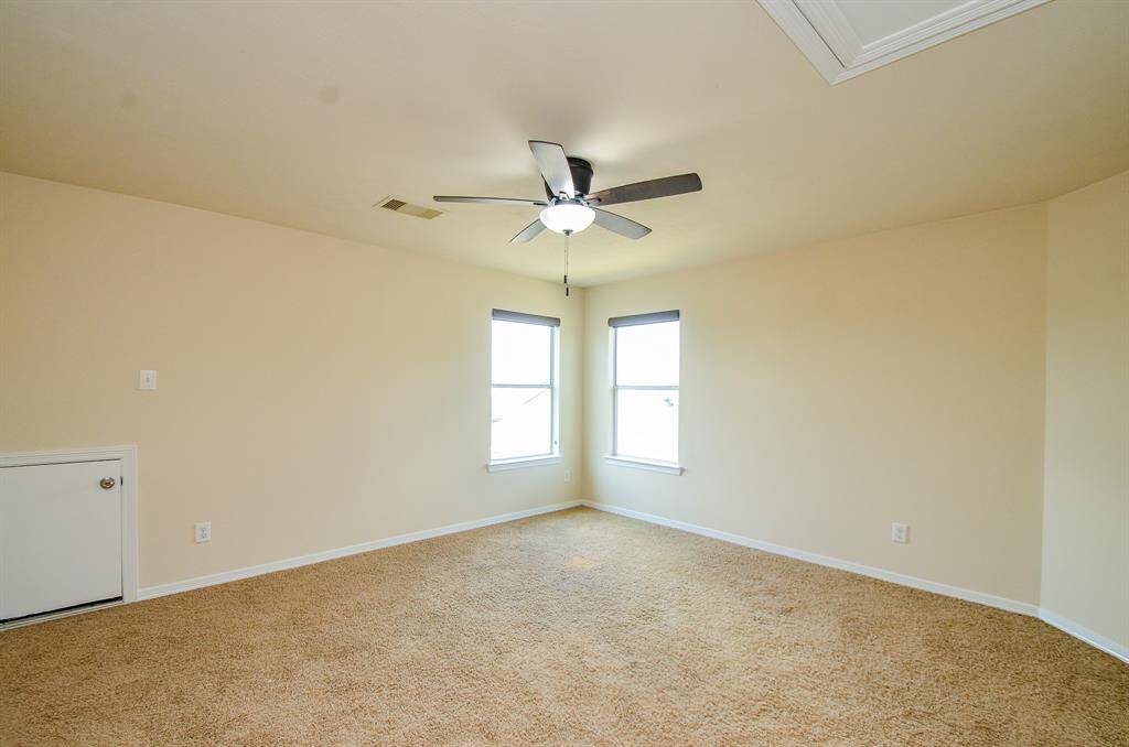 Spacious game room with neutral walls and carpet, featuring a ceiling fan and two windows for natural light.