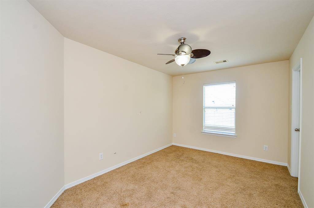 This secondary bedroom features neutral walls, carpeted flooring, a ceiling fan with light, and a window with blinds offering natural light. It's a versatile space suitable for a bedroom or office.