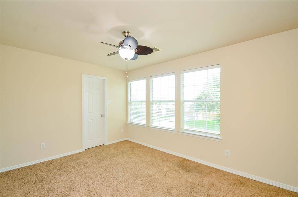This secondary bedroom features neutral walls, carpeted flooring, a ceiling fan with light, and a window with blinds offering natural light. It's a versatile space suitable for a bedroom or office.