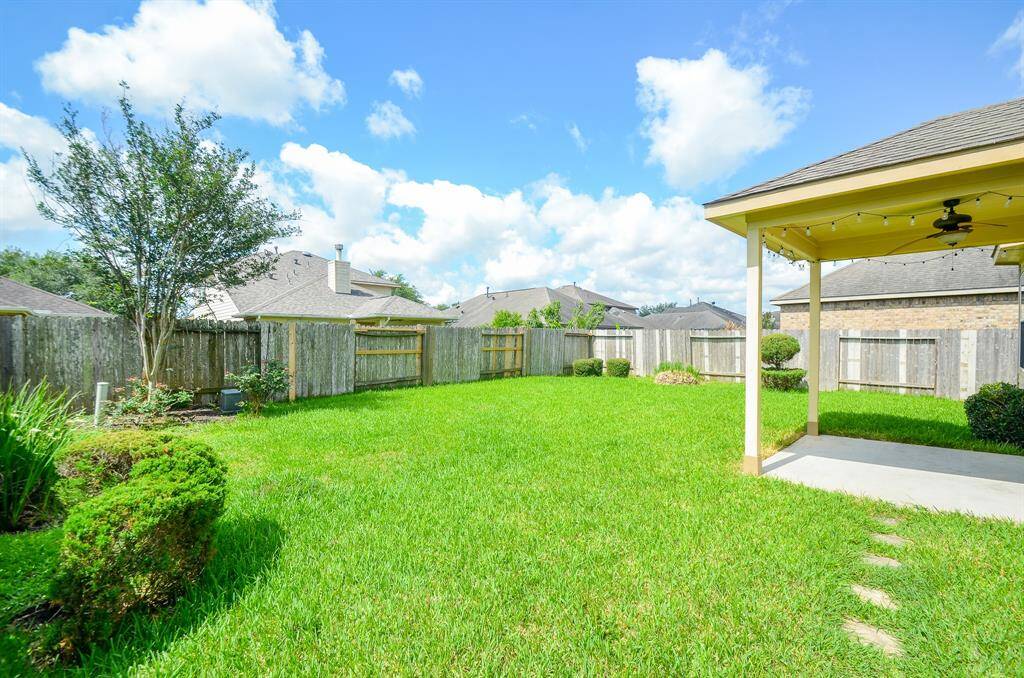 Spacious backyard with lush green lawn, privacy fencing, and a covered patio perfect for outdoor relaxation and entertainment.