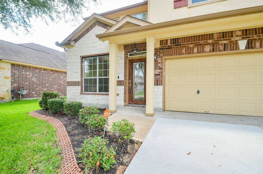 This home features a welcoming entrance with a covered porch, decorative brickwork, and a spacious attached garage. The well-maintained front yard includes neatly trimmed shrubs and a lush lawn, creating a charming curb appeal.