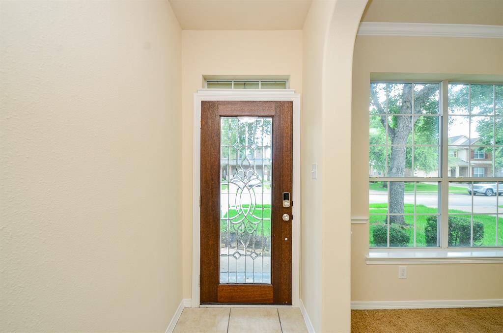 Bright and welcoming entryway featuring a decorative glass front door and large window, offering plenty of natural light and a view of the front yard.
