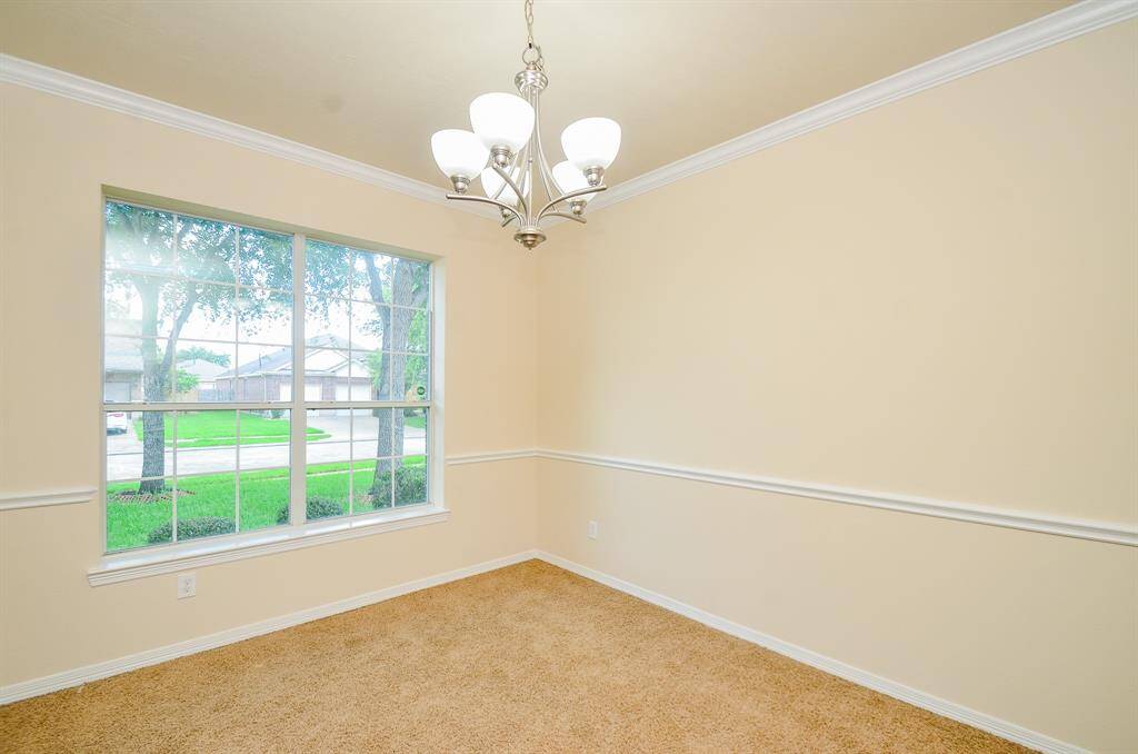 Bright dining room with a large window offering plenty of natural light. Features neutral walls, crown molding, and a modern chandelier, creating a welcoming atmosphere.