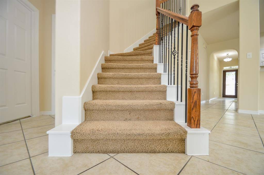 An inviting entryway and a carpeted staircase with elegant wooden railing details. The space is bright with neutral walls and tiled flooring, leading to a well-lit hallway.