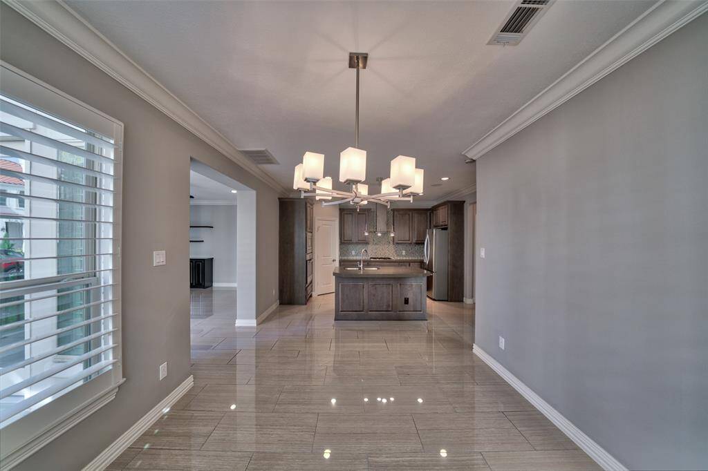 Another view of the dining room to showcase the open-concept kitchen and dining area. It features sleek tiled flooring, contemporary light fixtures, and large windows with shutters that provide ample natural light, enhancing the space's inviting atmosphere.