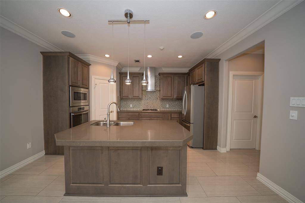 Modern kitchen with sleek cabinetry, a large central island with a sink, and stainless steel appliances. Recessed lighting and pendant lights add brightness, while neutral tones maintain the warm, inviting atmosphere.