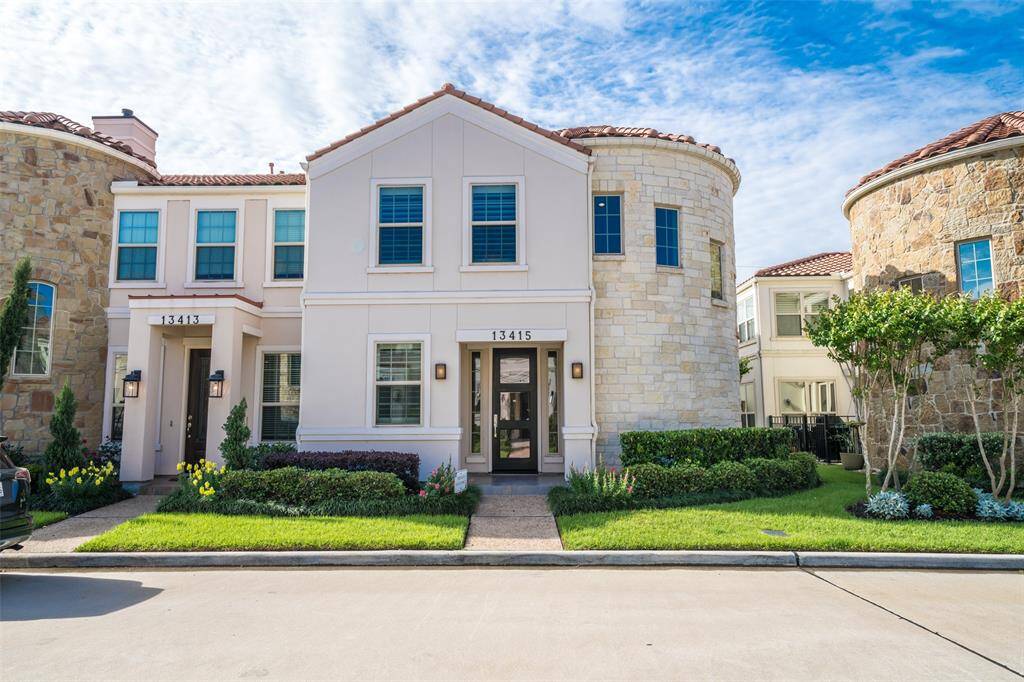 Two-story townhouse with a unique stone and stucco exterior. It features a well-maintained front yard with lush greenery and vibrant flowers. The home has a charming entrance and multiple windows for natural light.