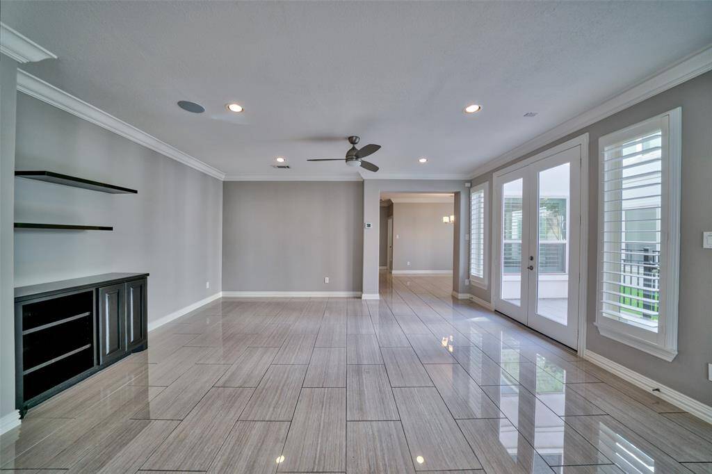Features include a ceiling fan, recessed lighting, built-in shelving, and large windows with plantation shutters offering natural light. The French doors open to the outdoor patio, perfect for entertaining and family gatherings.