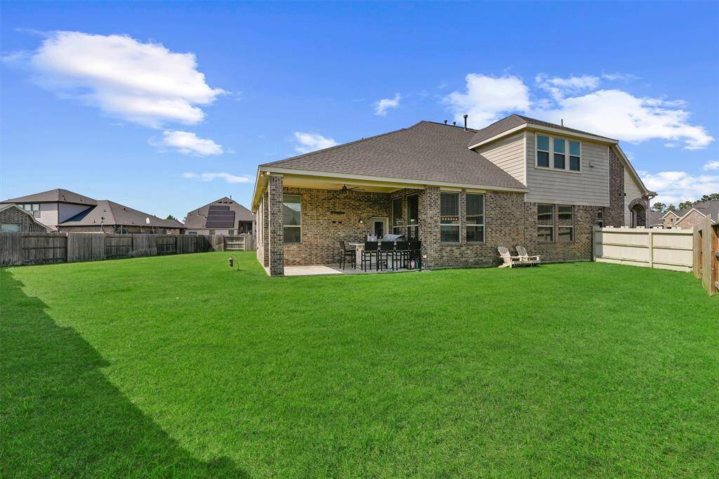 a covered patio with a ceiling fan and an outdoor kitchen setup, overlooking a well-maintained grassy backyard enclosed by a wooden fence. Ideal for outdoor entertaining and relaxation.