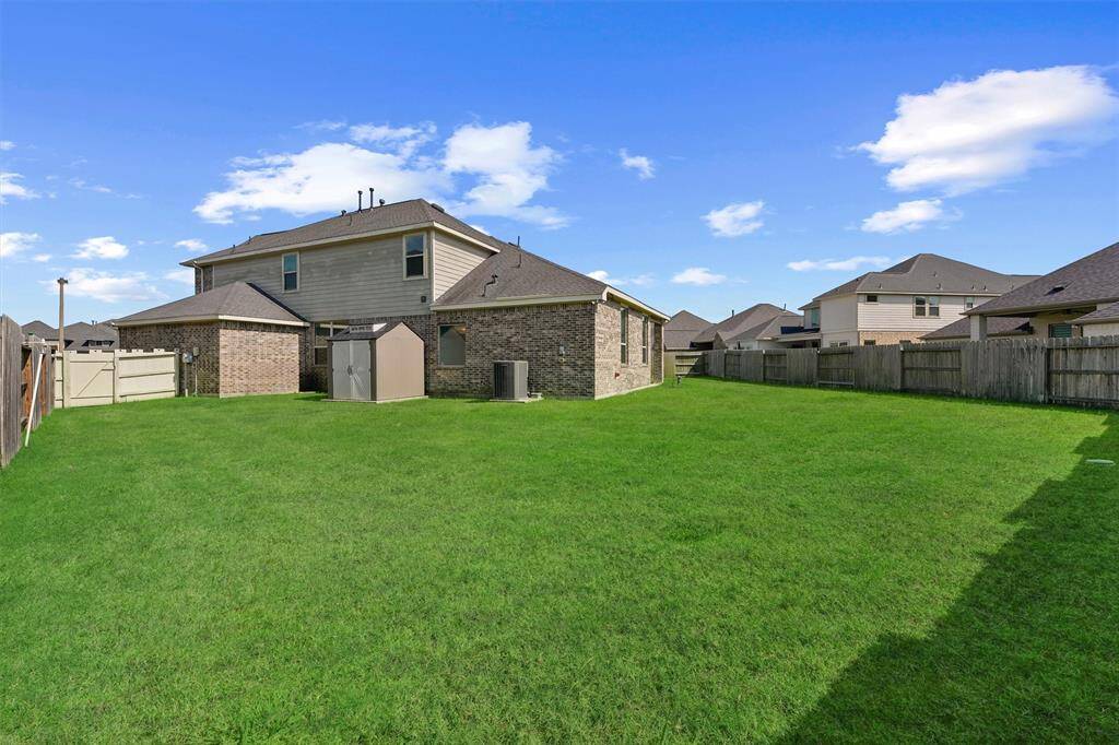 a covered patio with a ceiling fan and an outdoor kitchen setup, overlooking a well-maintained grassy backyard enclosed by a wooden fence. Ideal for outdoor entertaining and relaxation.