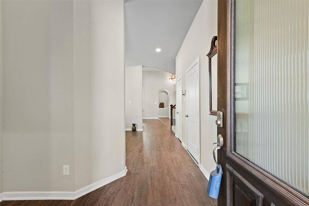 Welcome to a bright, inviting entryway featuring hardwood looking (tile) floors and neutral walls. The hallway leads to an open area with stylish lighting fixtures, offering a warm and spacious feel.