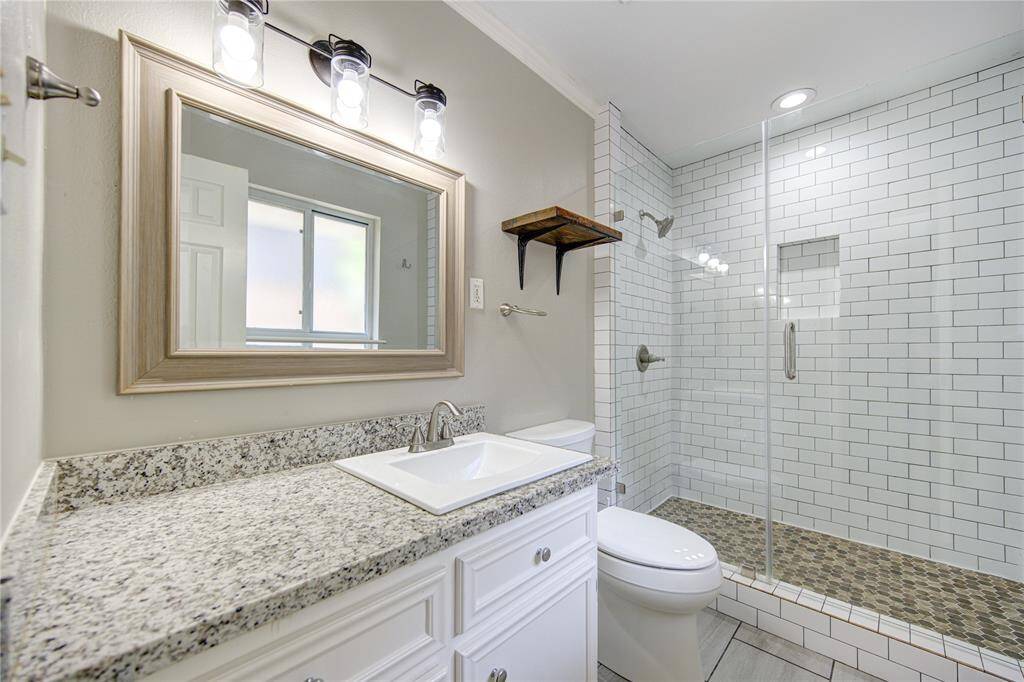 Primary bath with granite and frameless glass shower with subway tile