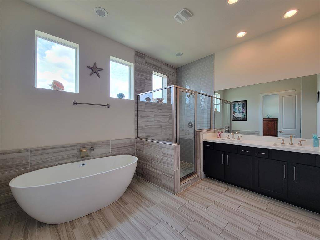 Modern bathroom with freestanding tub, walk-in shower, double vanity, and high windows providing natural light.