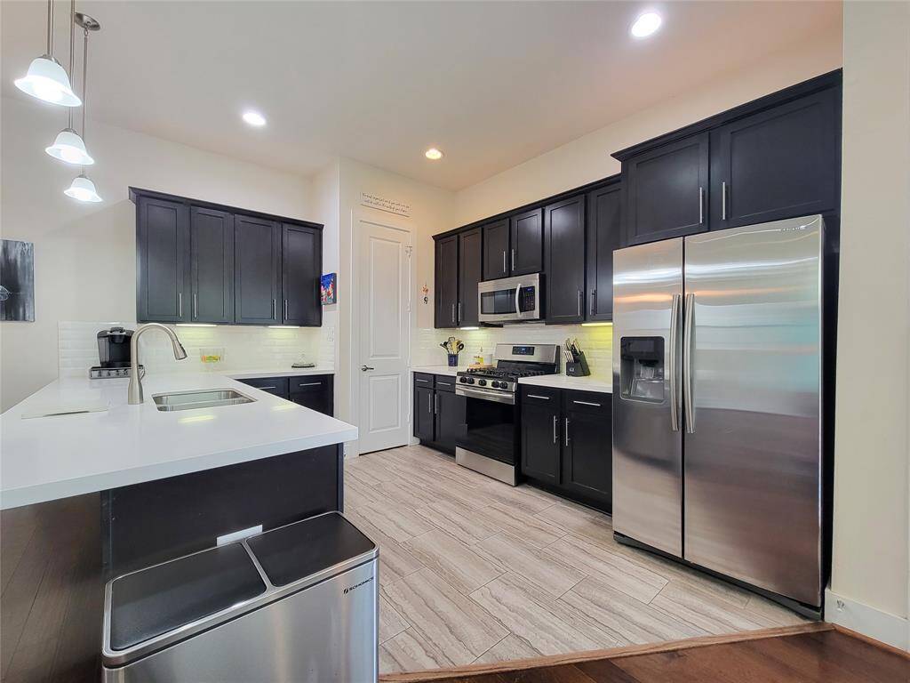 Modern kitchen interior with dark cabinetry, stainless steel appliances, white countertops, and pendant lighting.