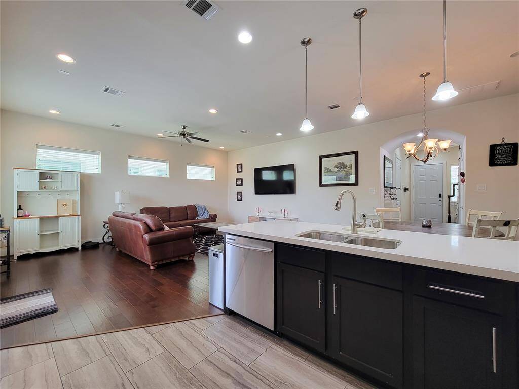 Modern open-plan living space with kitchen island, pendant lights, dining area, and hardwood floors.