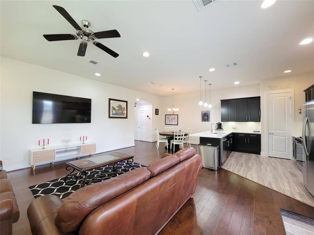 Modern open-concept living space with a kitchen, dining area, and living room with hardwood floors, black cabinets, and contemporary furnishings.