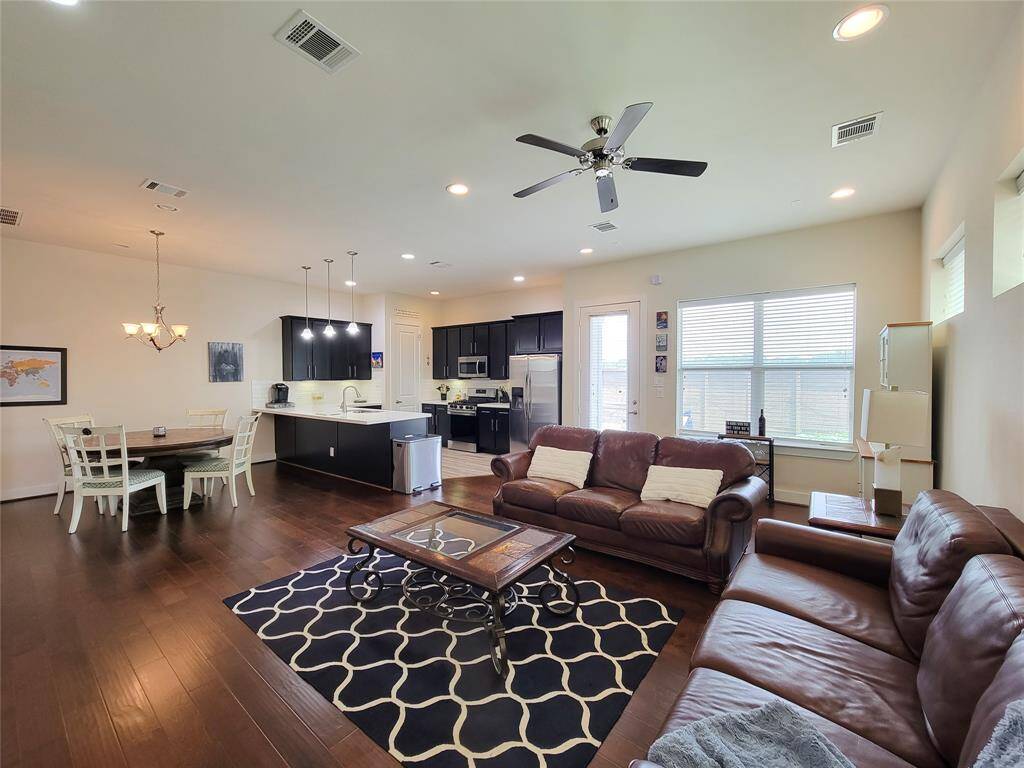 Modern open-plan living space with a kitchen, dining area, and living room, featuring dark wood floors and light-colored walls.