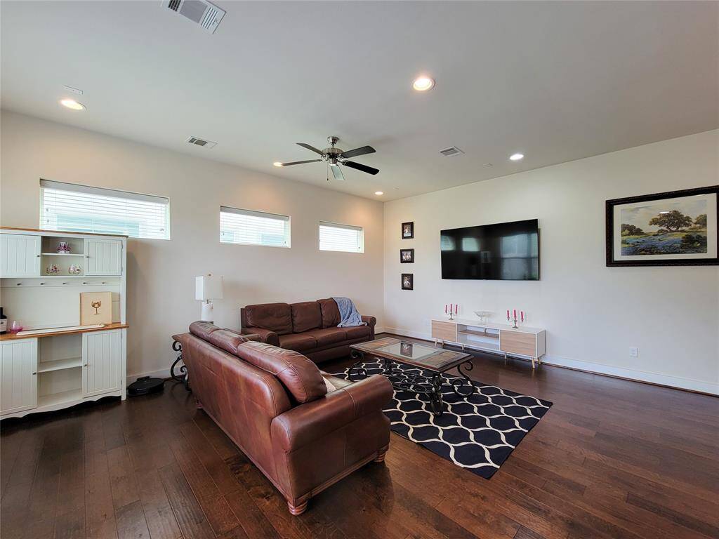 Modern living room with a leather sofa, hardwood floors, white walls, flat-screen TV, and minimalistic decor.