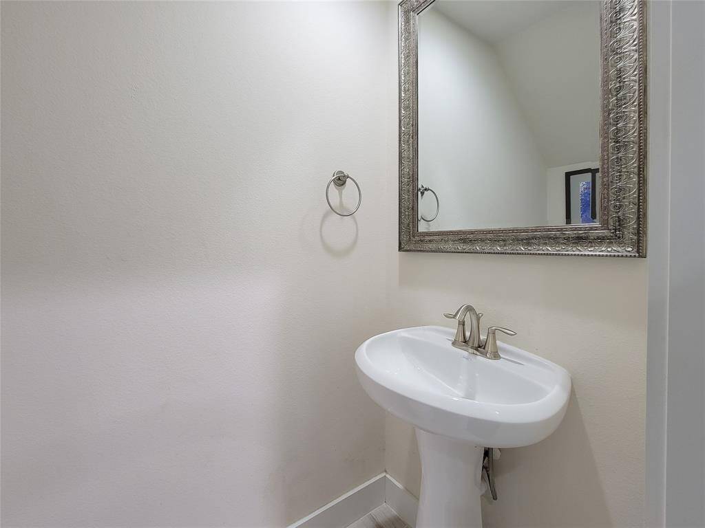 A clean, minimalist bathroom corner featuring a white pedestal sink and a decorative mirror on a neutral wall, with a towel ring to the side.