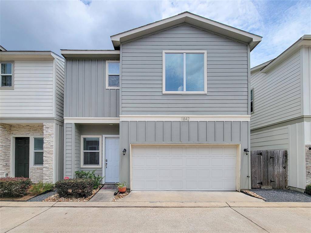 A two-story townhouse with gray siding, a 2-car garage, and a small landscaped front yard.
