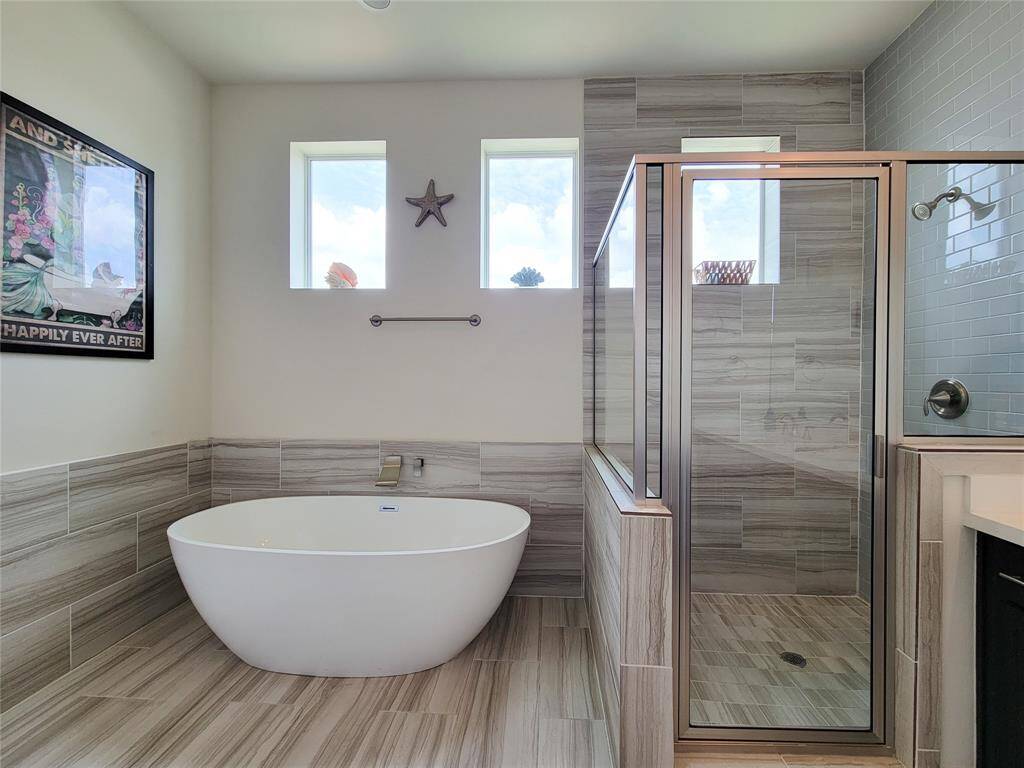 Modern bathroom with freestanding tub, glass shower stall, and gray tile.