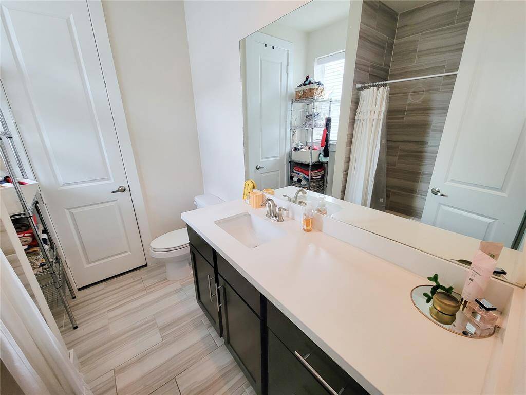 Modern bathroom with a double sink vanity, large mirror, tiled shower, and a view into an adjoining closet.