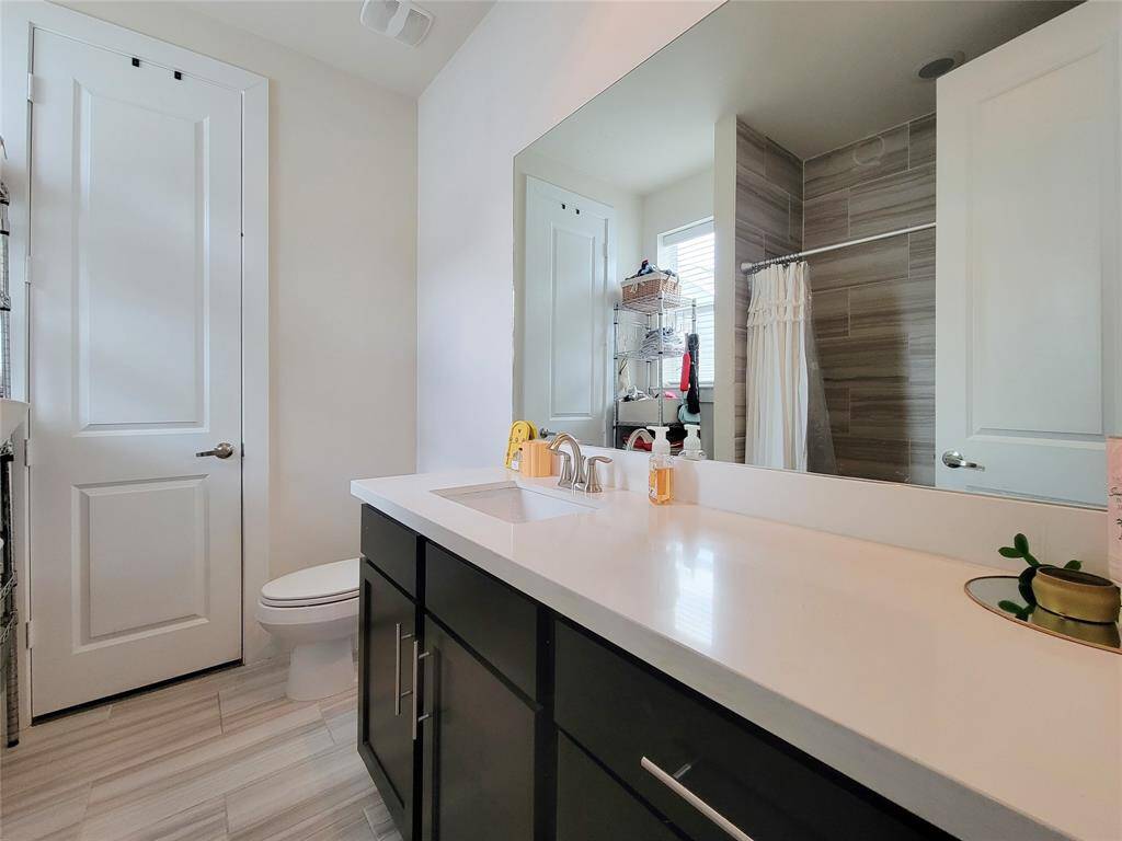 A modern bathroom with a large vanity, mirror, toilet, and a shower with a curtain. Bright and clean with neutral colors.