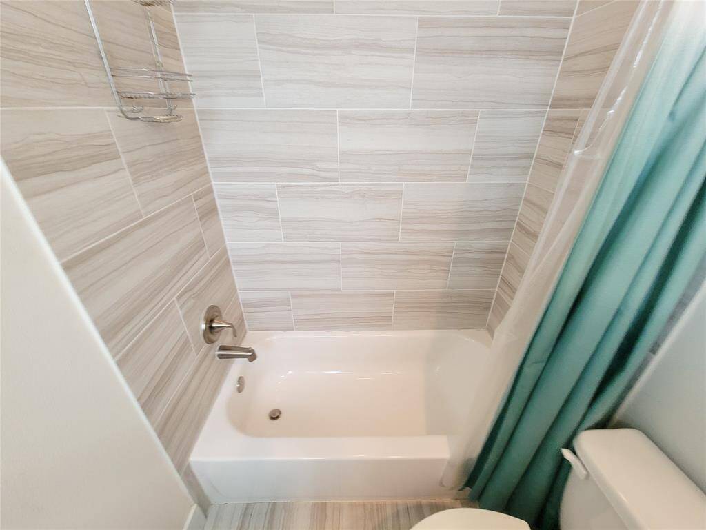 Middle bathroom with a white bathtub, tiled walls, tand a toilet.