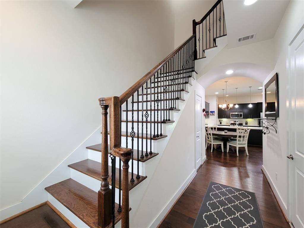 A well-lit interior with a wooden staircase leading upstairs, a view into a kitchen with a dining area, and modern design elements.