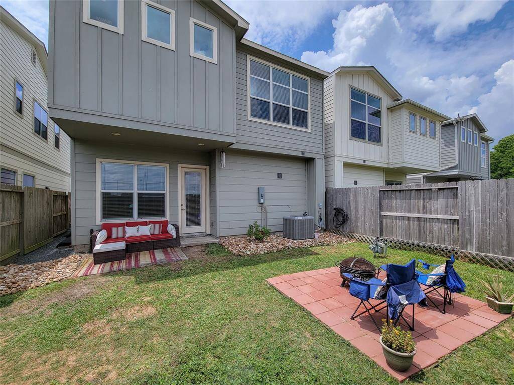 A backyard with a small patio, lawn, outdoor furniture, and the rear view of a modern two-story house with a wooden fence.