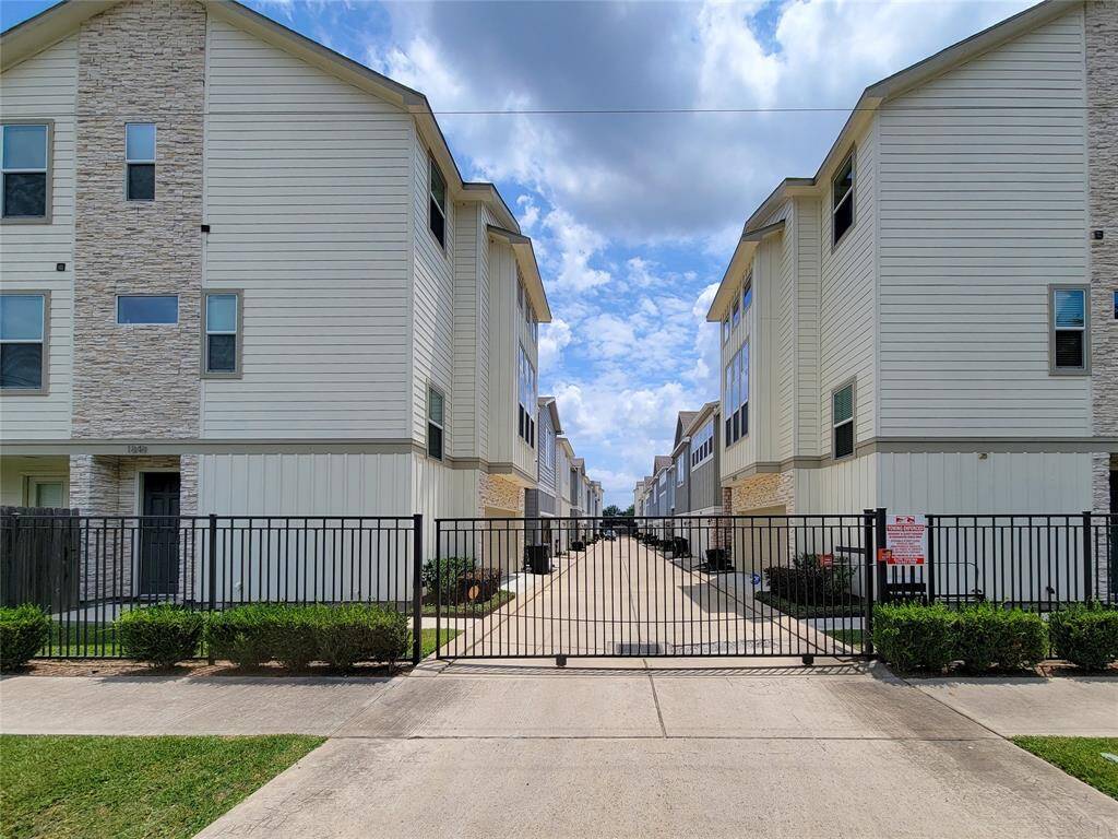Symmetrical view of a residential complex with identical multi-story buildings, a central walkway, iron gate, clear sky.