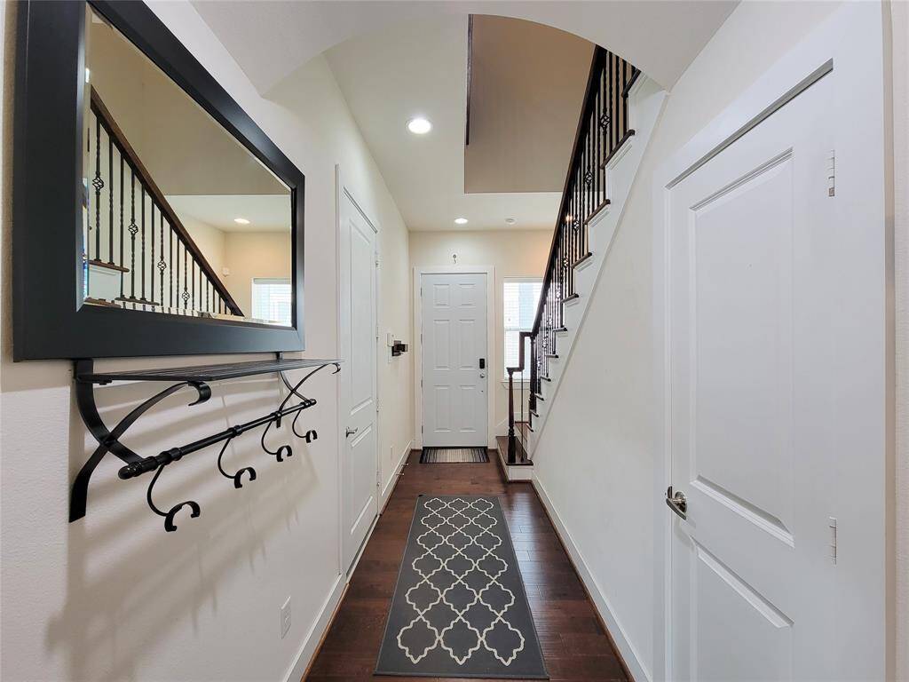 A modern hallway with dark wood floors, white walls, a staircase with metal balusters.