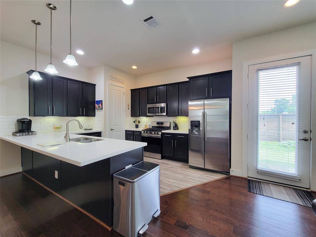 Modern kitchen interior with dark cabinets, stainless steel appliances, an island, pendant lights, and a door leading outside.