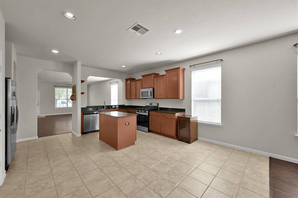 Light tile flooring, plenty of natural light from a large window, and warm wood cabinetry. It includes modern stainless steel appliances, a central island, and ample counter space, perfect for cooking and entertaining.